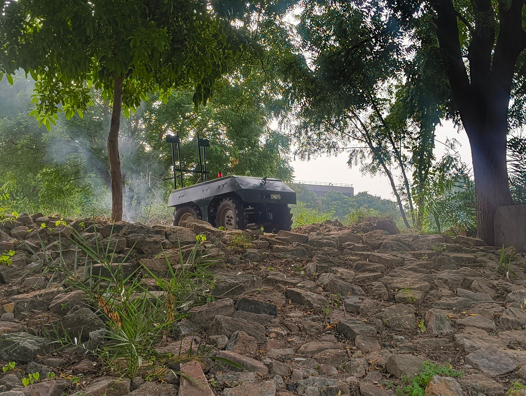 Agrover electric rover traversing a rocky slope beneath trees.